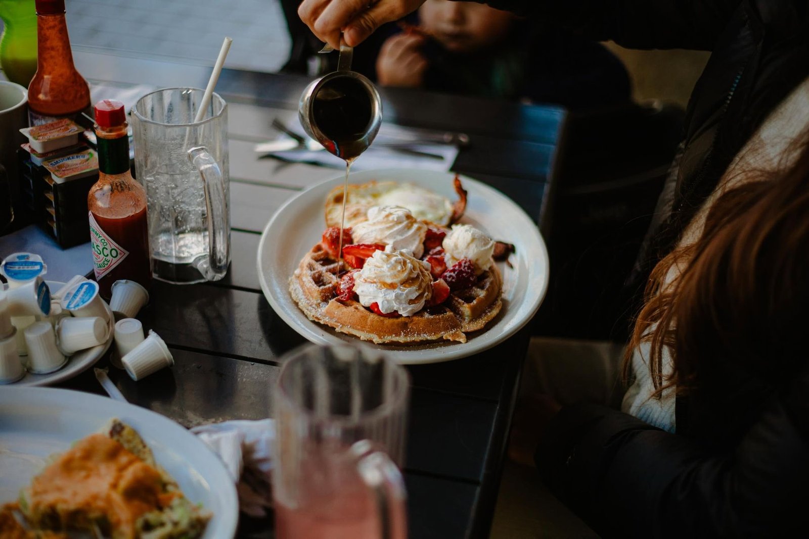 Belgian waffle with strawberries and whipped cream, syrup being poured